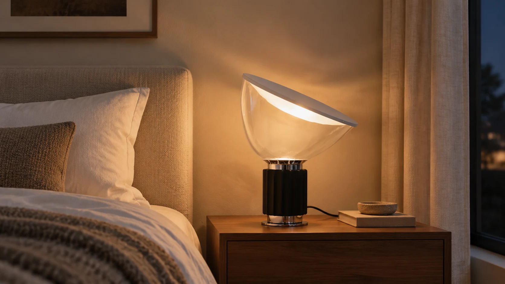 Illuminated black Taci table lamp beside a bed at night