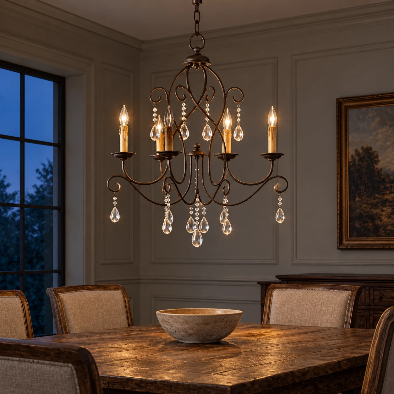 Four-light iron chandelier glowing above a dining table at dusk