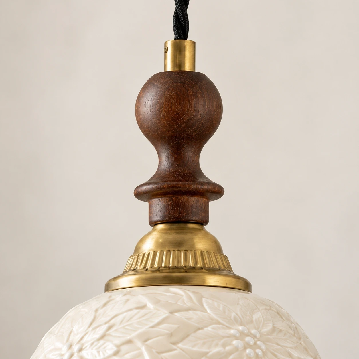 Close view of the black twisted cord, solid-wood ornament, and brass-tone connectors