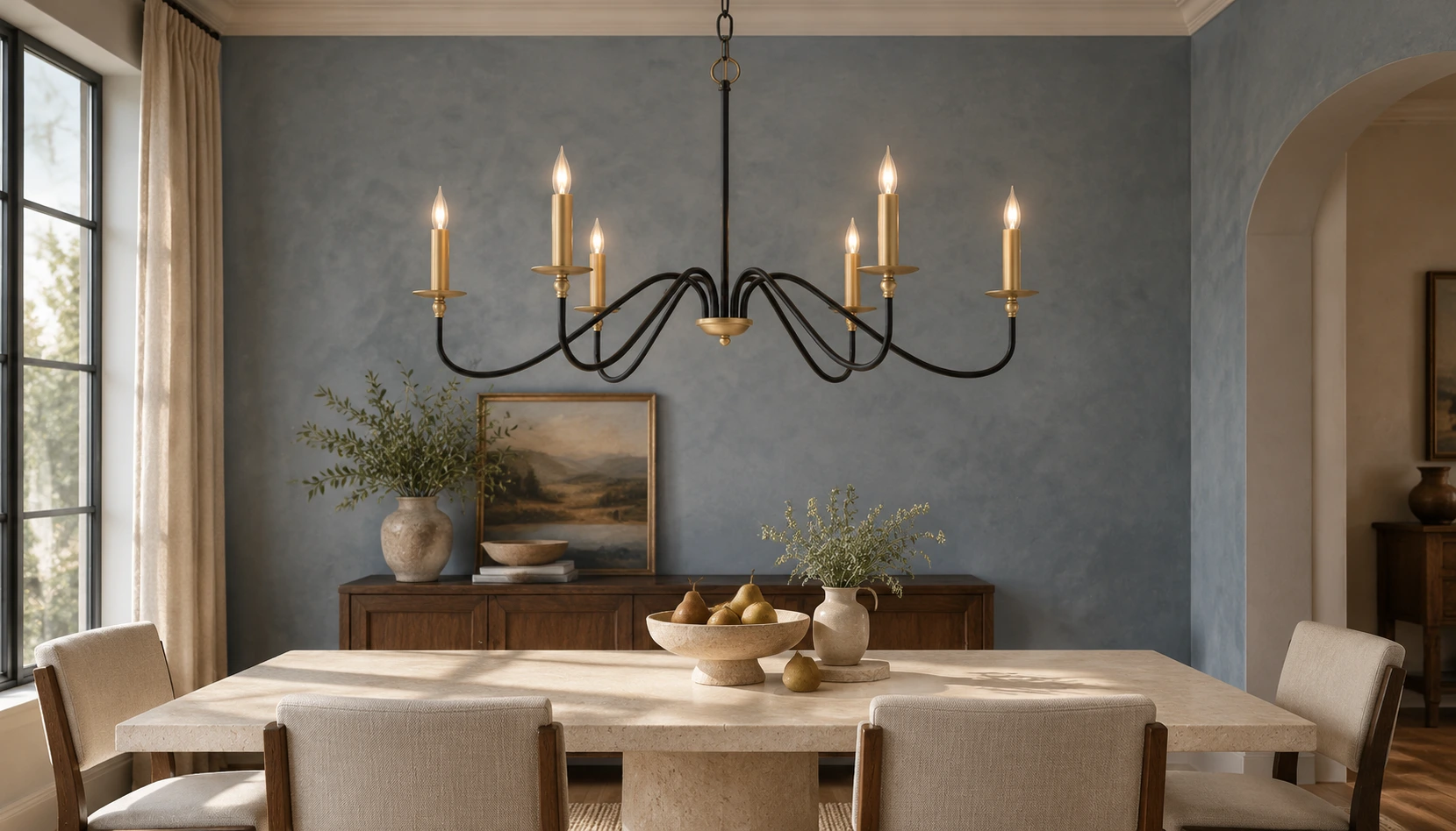 Arden vintage black iron chandelier illuminated above a pale limestone dining table in a slate-blue transitional room